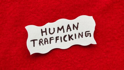 Human Trafficking word letters text handwritten calligraphy design on white paper label note isolated on a red background surface with copy space. Closeup macro top view. Human Trafficking concept.