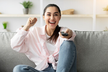 Cheering. Excited woman watching sport on TV at home, celebrating success, raising up and shaking...