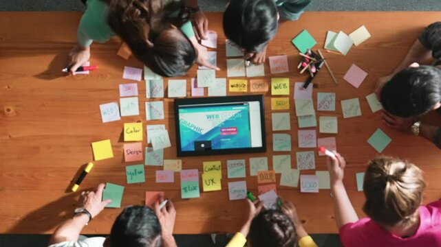 Top down view of programmer brainstorming and planning about web design while looking at tablet wireframe prototype. Aerial view of skilled developer team talking about digital application. Symposium.