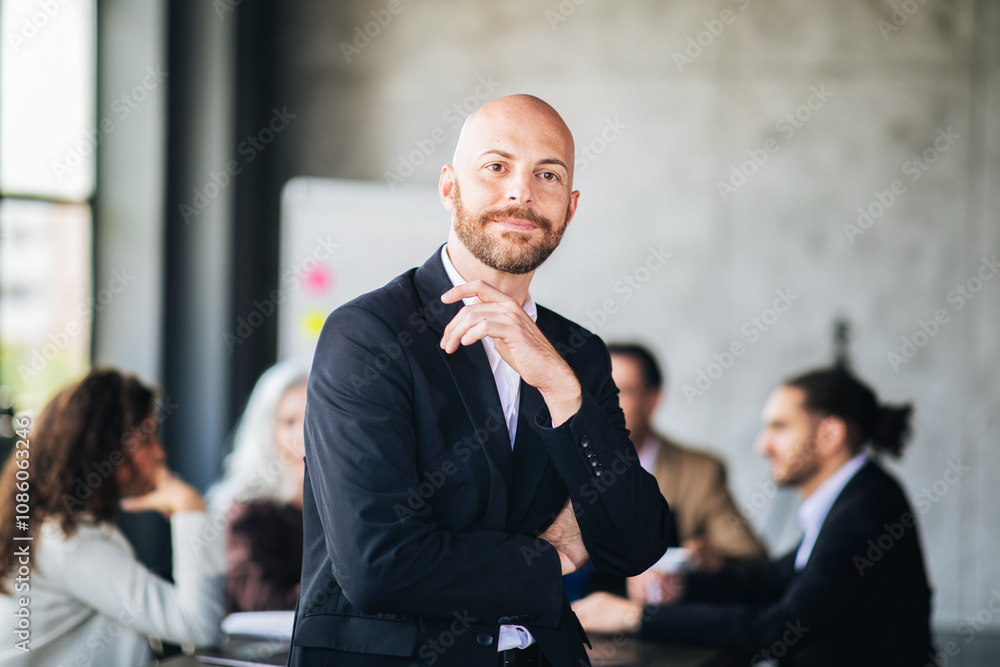 Aufkleber a young man with a beard confidently poses in a stylish suit at a meeting table while colleagues eng