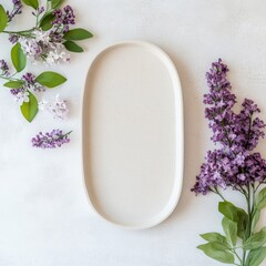 Elegant arrangement of fresh lilac flowers with a minimalist oval plate on a light background