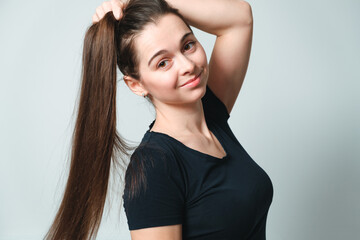 Portrait of beautiful smiling 30 years woman holding her long brown hair with hand on grey background. Pretty girl face. Looking at camera. European appearance. Healthy natural hair without coloring