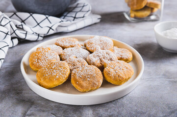 Sweet pumpkin cookies in powdered sugar on a plate on the table