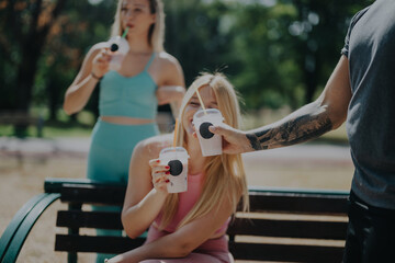 A group of friends casually enjoying smoothies while relaxing in a sunny park. This image captures...