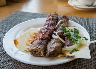 Lula kebab, on lavash, with red onion, pomegranate, and sumac, close-up, horizontal, no people,
