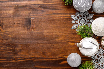 A flat lay of stylish Christmas ornaments, including silver and white baubles with pine branches on wooden background with copy space top view for festive decoration