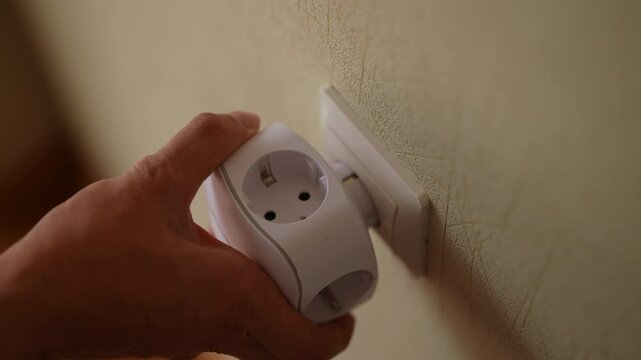 Close-up top view of unrecognizable electrician male inserting white electrical outlet tee or triple adapter into wall socket, enhancing electrical access and convenience. Shooting in slow motion.