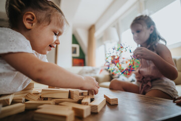 Young girls engaging in creative play with wooden blocks and a colorful toy indoors, showcasing childhood fun and imagination.