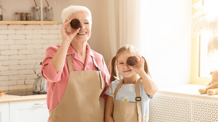 Baking is fun. Senior lady and her grandchild with chocolate muffins being silly in kitchen, empty space