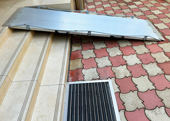 An aluminium portable ramp positioned over a staircase and onto a tiled surface, designed to ensure...
