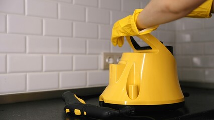 Fototapeta premium Steam cleaner for cleaning ceramic tiles in the kitchen. Close-up of the steam cleaner and a woman's hand. Home cleaning services.