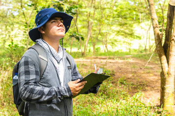 A botanical engineer seriously analyzes the treetops while holding a notebook for taking notes,...