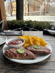 Grilled Steak with Herb Butter, Crispy Fries, and Tomato Sauce on a Rustic Outdoor Table