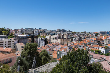 Panoramic view of Lisbon cityscape, showcasing terracotta rooftops, traditional and modern architecture under a clear blue sky. Lisbon, Portugal.