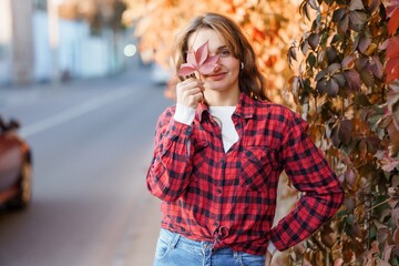 Fototapeta premium Young Woman Playfully Posing with Autumn Leaf Against Colorful Foliage Background