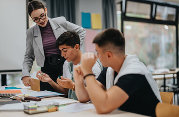 A teacher engages with two students during a classroom activity, fostering learning and collaboration. The setting is a bright and interactive educational environment focused on student participation.