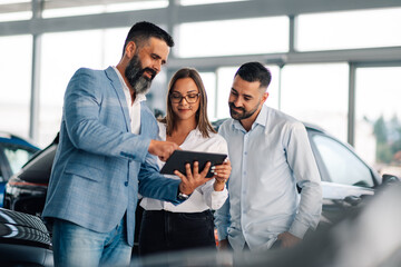 Professionals review car options on a tablet in dealership space.