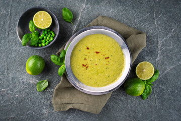 Fresh spicy creamy green pea soup pureed blend with lime and basil served as top view in a design bowl