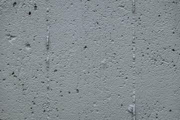 A detailed close-up of a rough, porous concrete surface. The texture features small holes and...