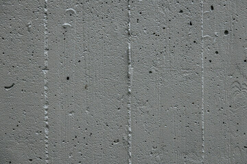 A detailed close-up of a rough, porous concrete surface. The texture features small holes and cracks, showcasing the raw and industrial appearance of the material.