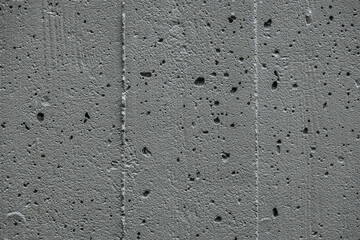 A detailed close-up of a rough, porous concrete surface. The texture features small holes and cracks, showcasing the raw and industrial appearance of the material.