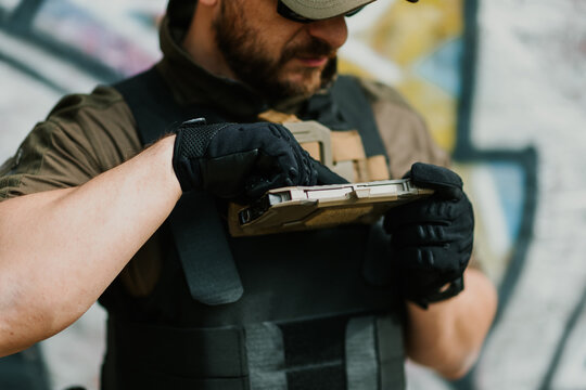 Soldier wearing tactical vest and gloves using tablet computer in urban environment