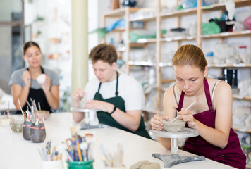 Teenage girl attentively learns how to make pottery with a wooden sticker in the workshop