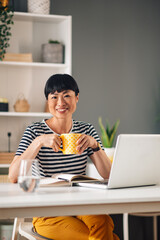 Asian woman holding a yellow cup while sitting at her work desk.