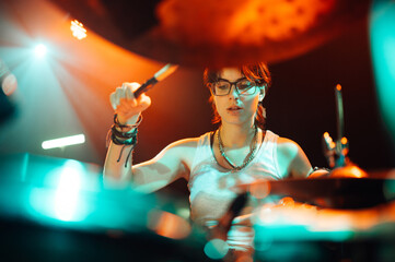 Female drummer performing live on stage with colorful lighting