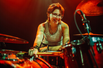 Drummer playing drums on stage with red backlight