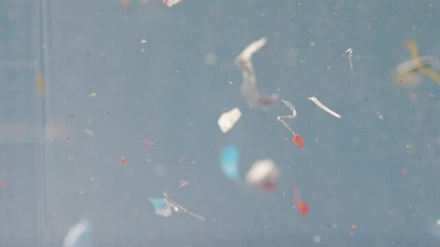 Colorful microplastics swirl in water in a close-up view, emphasizing contamination and the ecological issue of waste pollution.