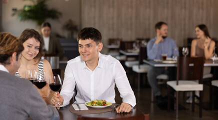 Couple young guy and woman and adult man eating drinking wine and talking in restaurant
