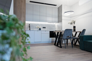 Modern kitchen interior with kitchen furniture, dining table, chairs and wooden floor. Design indoors architecture in new apartment. Real estate.
