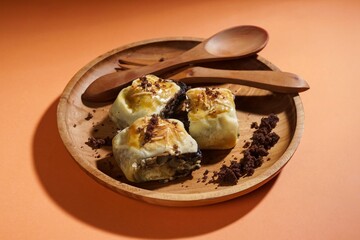 Banana bolen is made from banana peels and dry cakes and filled with chocolate and cheese. Served on a wooden plate. Selective focus image.