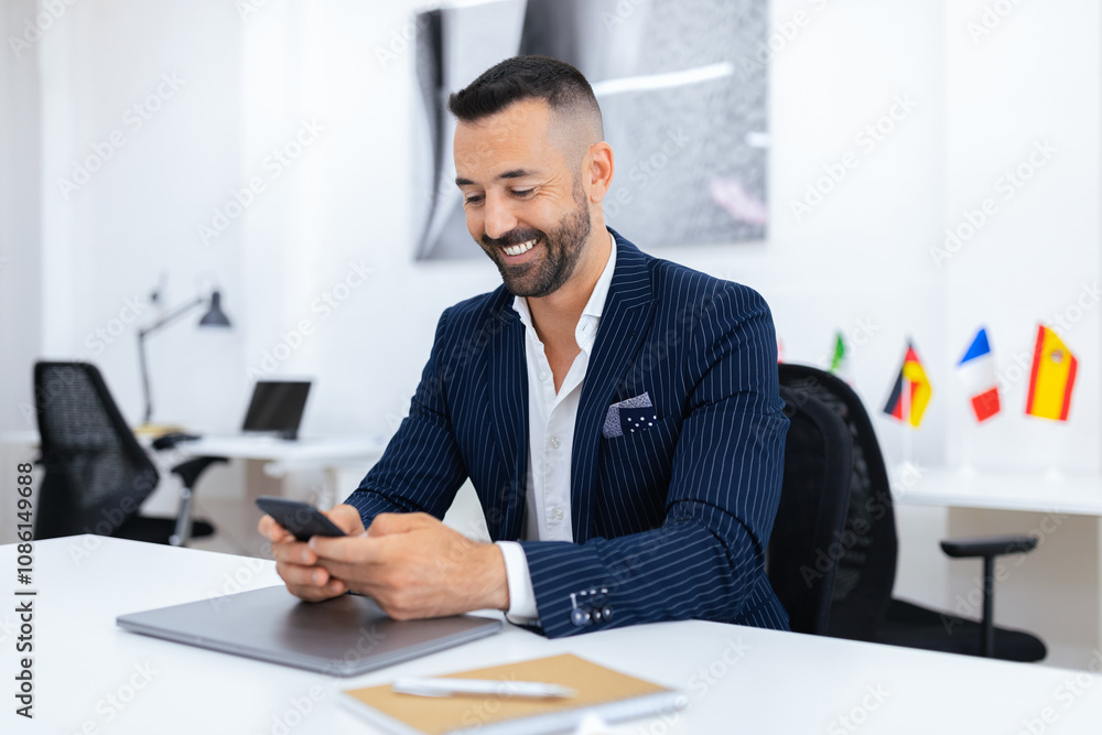 Poster a well-dressed man smiles while using his smartphone at a sleek office desk, decorated with national
