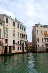 A view of historic Venetian buildings along the Grand Canal, showcasing classic Italian architecture. The iconic canal waters reflect the facades, with boats and gondolas adding to the charm of Venice