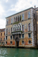 Obraz premium A view of historic Venetian buildings along the Grand Canal, showcasing classic Italian architecture. The iconic canal waters reflect the facades, with boats and gondolas adding to the charm of Venice