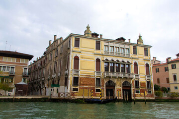 A view of historic Venetian buildings along the Grand Canal, showcasing classic Italian architecture. The iconic canal waters reflect the facades, with boats and gondolas adding to the charm of Venice