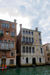 Naklejka premium A view of historic Venetian buildings along the Grand Canal, showcasing classic Italian architecture. The iconic canal waters reflect the facades, with boats and gondolas adding to the charm of Venice