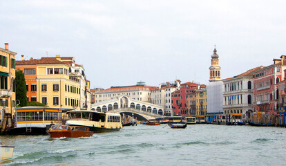 A view of historic Venetian buildings along the Grand Canal, showcasing classic Italian architecture. The iconic canal waters reflect the facades, with boats and gondolas adding to the charm of Venice