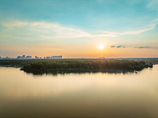 Big lake with green shores in bright sun light and city on horizon, aerial landscape. Recreation concept. Aerial view