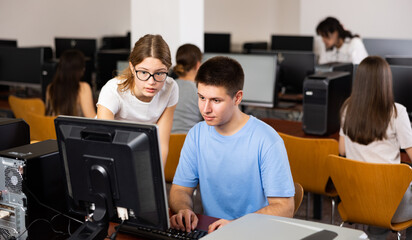 Fototapeta premium Concentrated female student explaining the topic to male friend while she is studying computer science on the pc in the classroom.