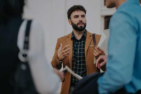 A group of business people engage in a dynamic meeting in a bustling city environment, showcasing communication, teamwork, and collaboration.