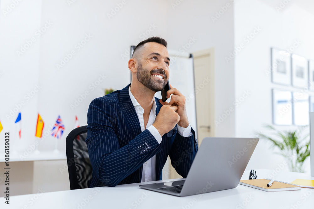 Poster a smiling businessman is speaking on the phone at his desk, surrounded by flags and modern decor. he
