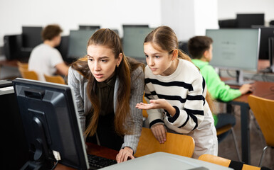 Positive woman teacher together with the girl teaches how to work on the computer