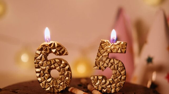 Number 65 year in golden candles shape in a chocolate cake. A homely atmosphere of a happy Birthday party. Garlands, paper caps and candle lights create comfort and warmth