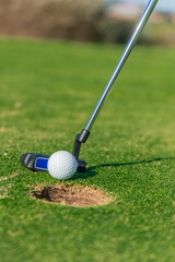 vertical close-up of putter and golf ball near hole on the green