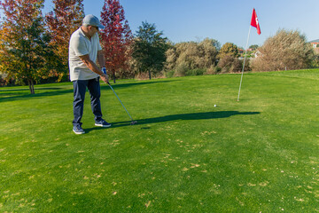 Senior golfer aiming with a putter on the green to guide the ball into the hole