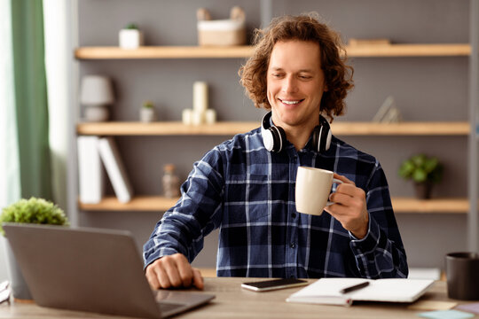 Successful Millennial Businessman At Laptop Drinking Coffee Enjoying Work Sitting At Workplace. Young Empolyee Worker Using Computer In Modern Office. Business People And Entrepreneurship