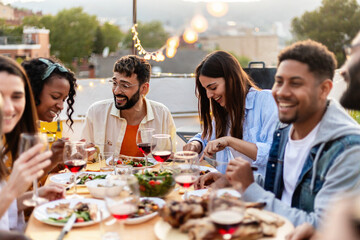Happy diverse group of friends enjoying dinner barbecue and drinking wine in summer at home terrace